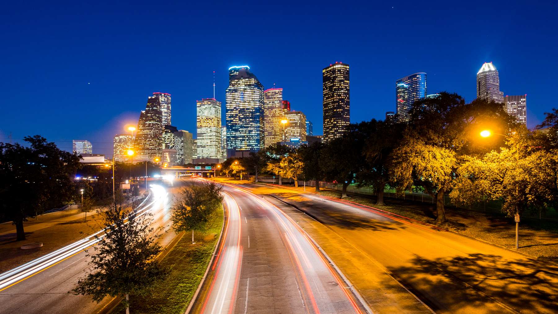 Traffic moving along a Houston highway at night with the downtown skyline behind it