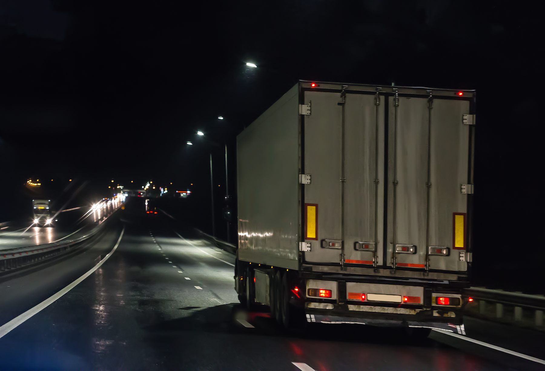 The rear of a tractor-trailer traveling on a wet highway at night