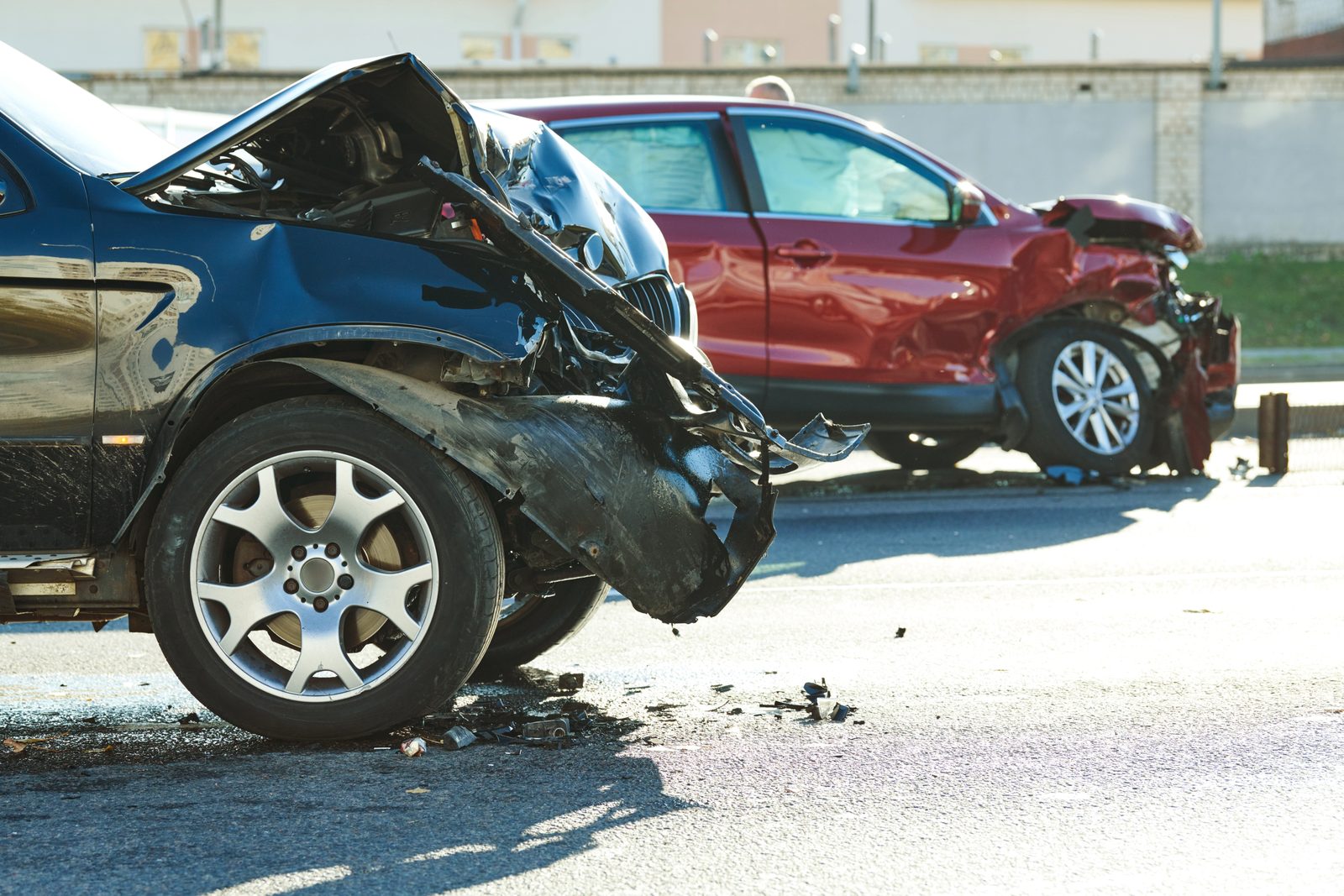 Two cars with heavy front-end damage stopped in the road after a collision, with debris scattered across the asphalt