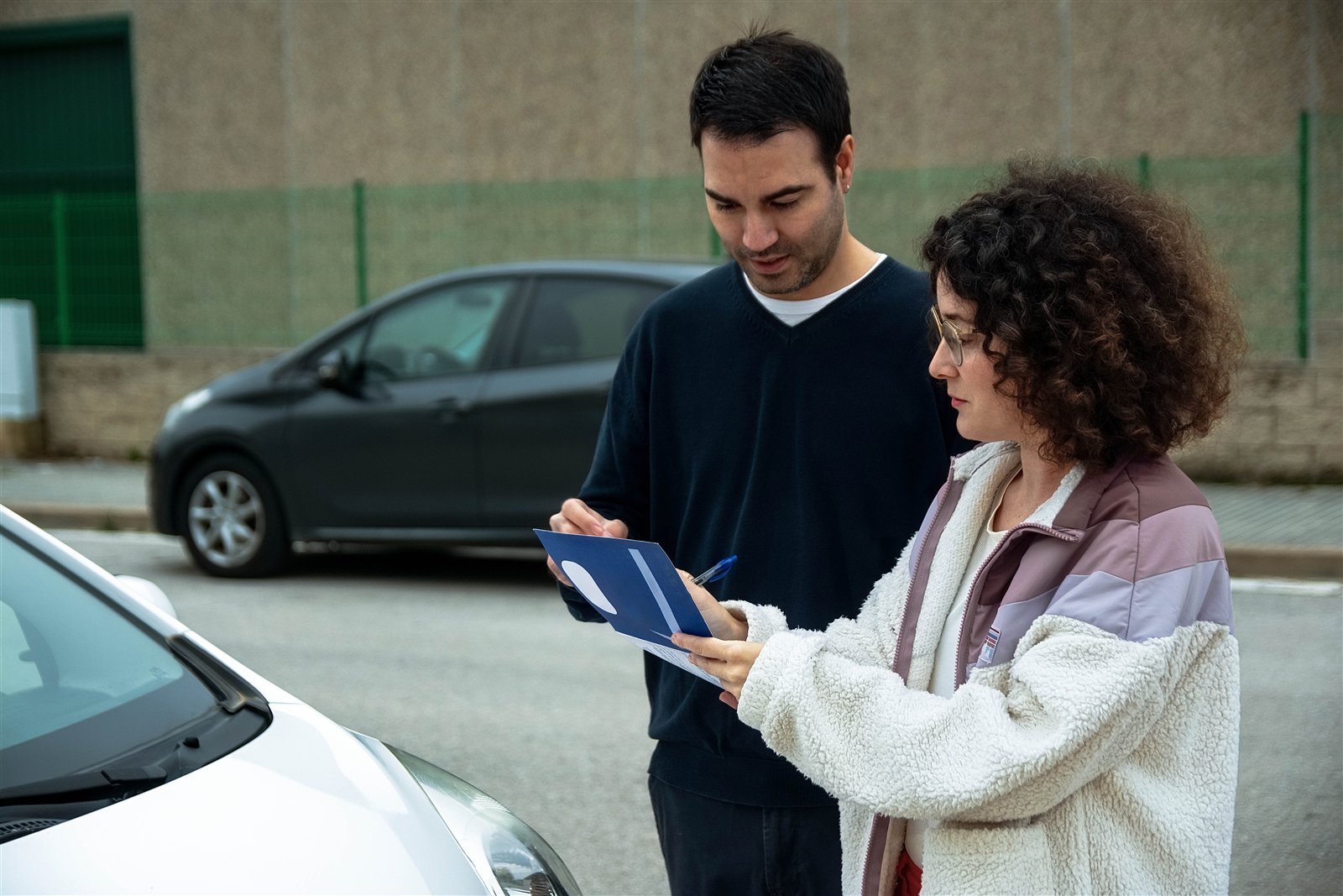 A couple standing beside a car at the roadside, looking at a tablet together after a collision