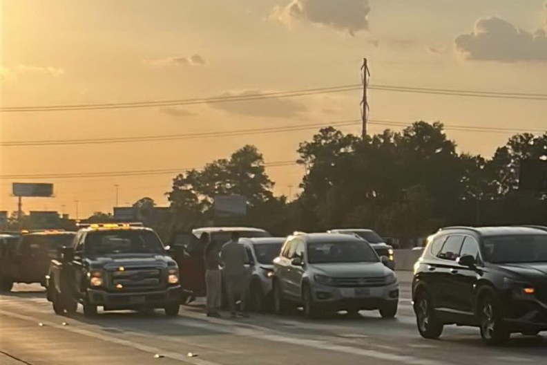 Traffic stopped across a Houston freeway at sunset, with hazard lights on.