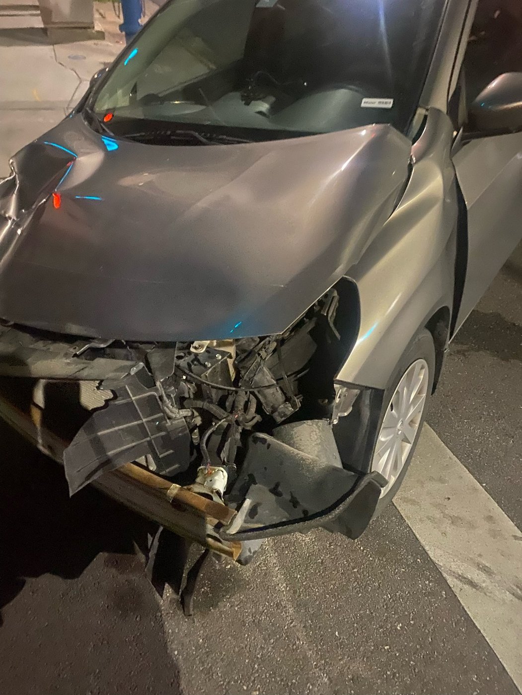 The front end of a sedan torn open, with the bumper and headlight assembly hanging loose, after a company van ran a red light.