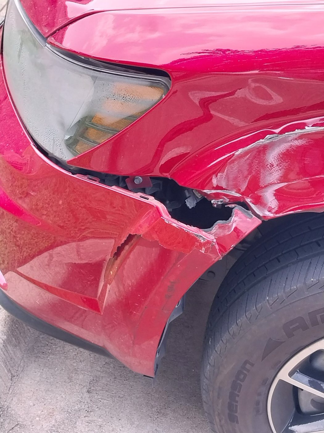 Crumpled front fender and headlight corner of a red SUV.