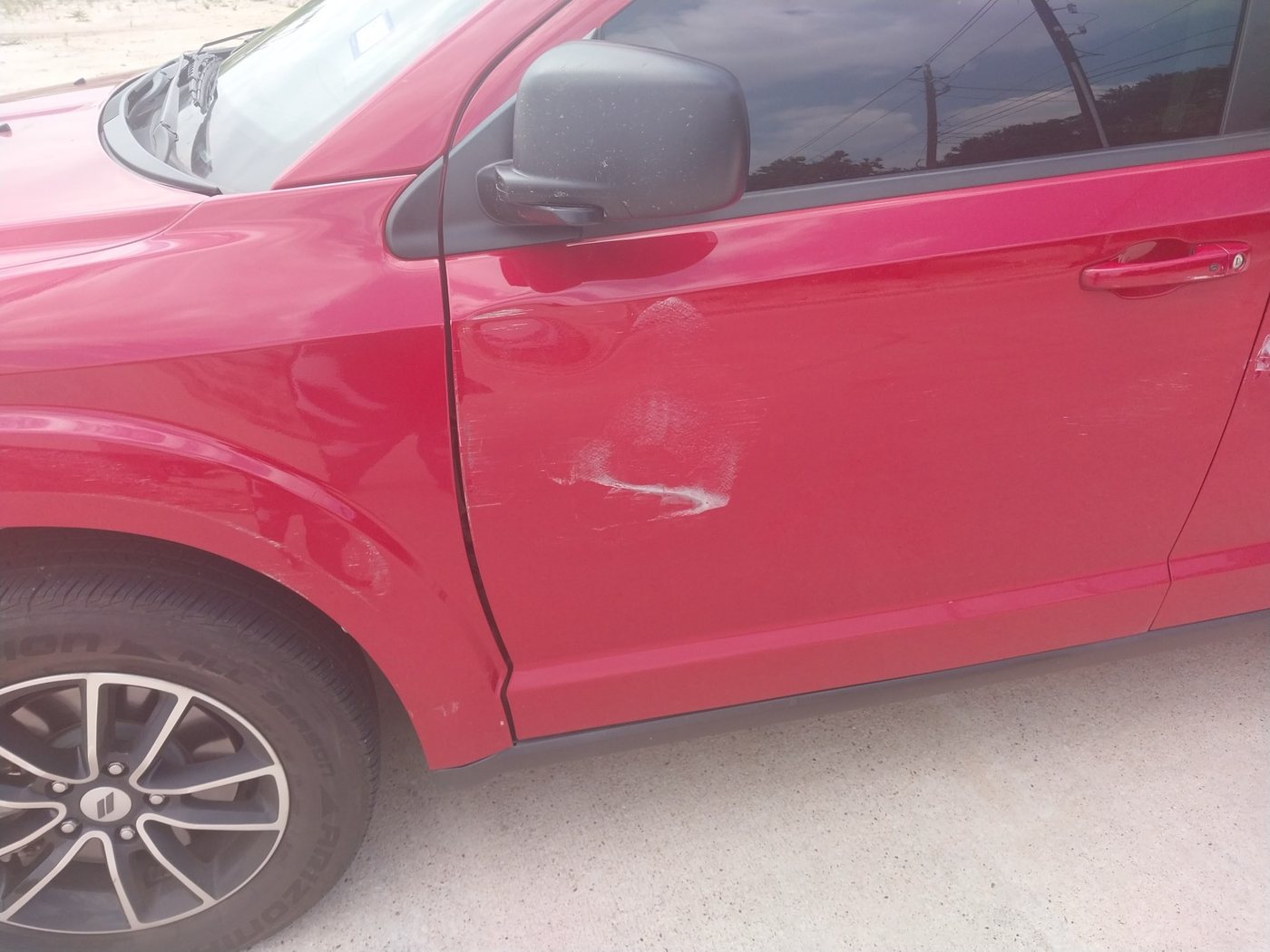 Crease and scrape running the length of the driver's side doors of a red SUV after a lane-change collision.