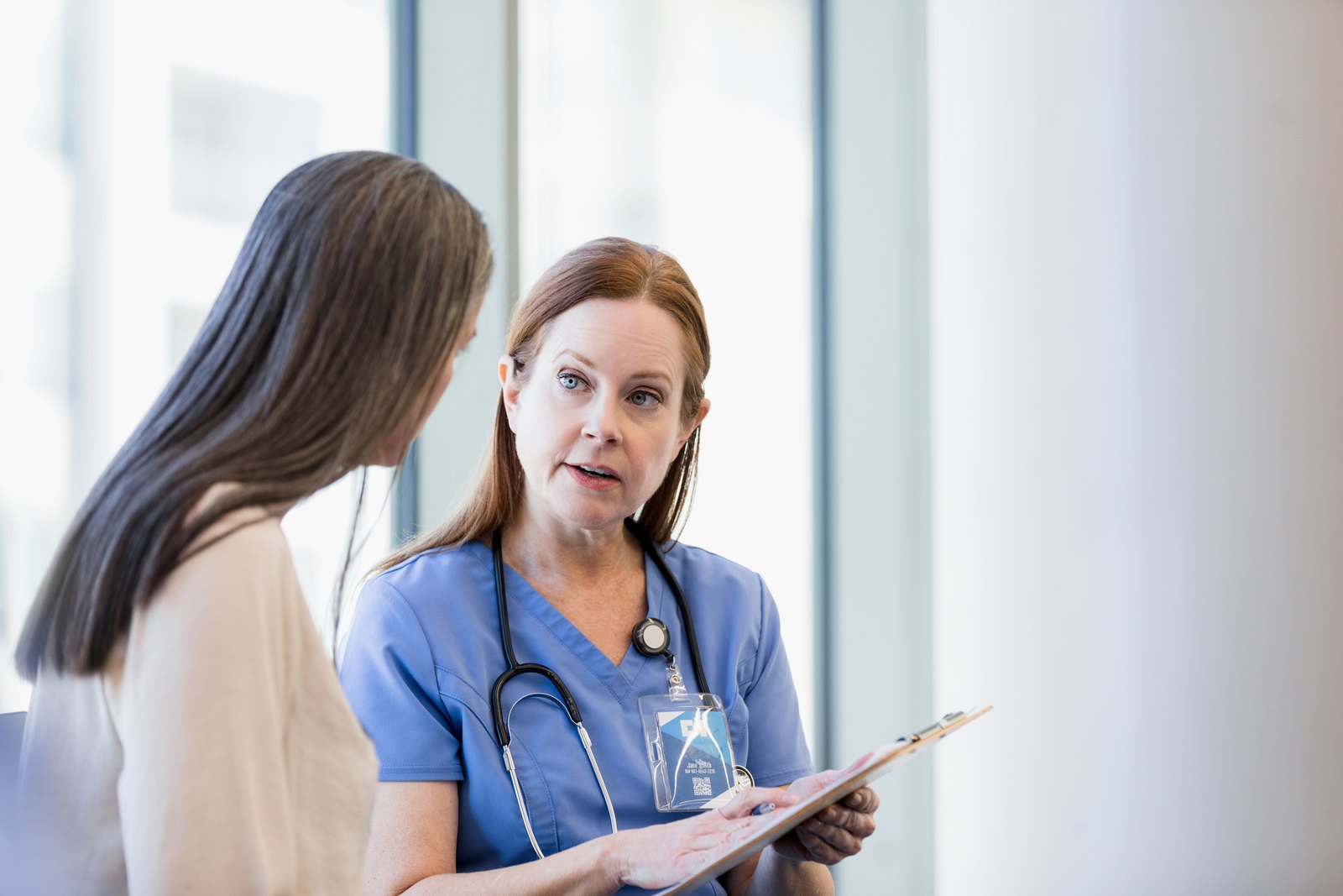 A clinician holding a clipboard explains test results to a patient during a consultation