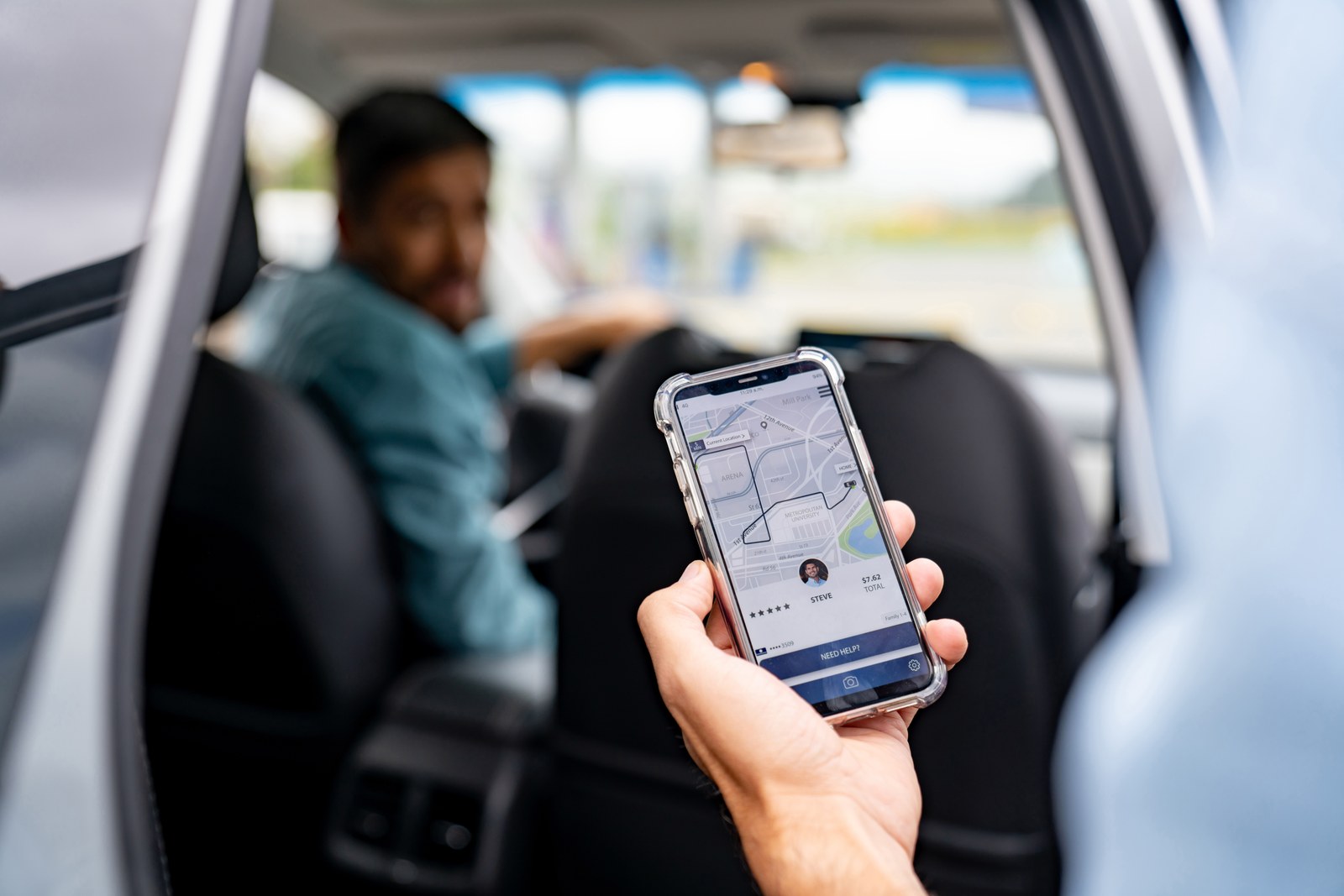Passenger in the back of a rideshare car in Texas holding a phone showing the ride app and driver details