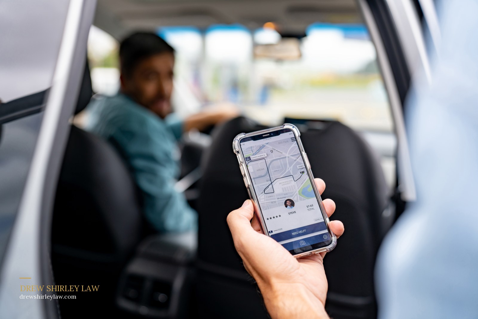 A passenger in the back of a rideshare car holding a phone showing the trip in progress