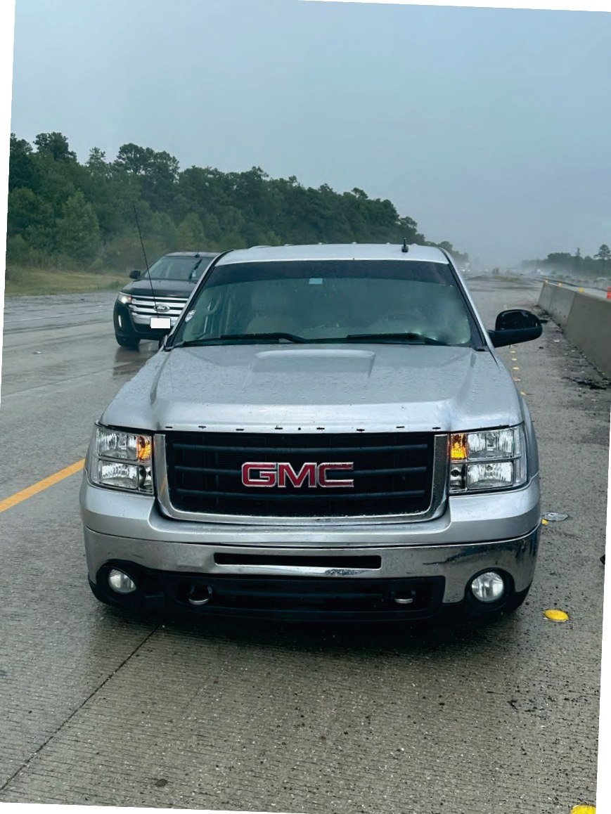 A silver pickup stopped on a wet freeway after being struck by a tractor-trailer.
