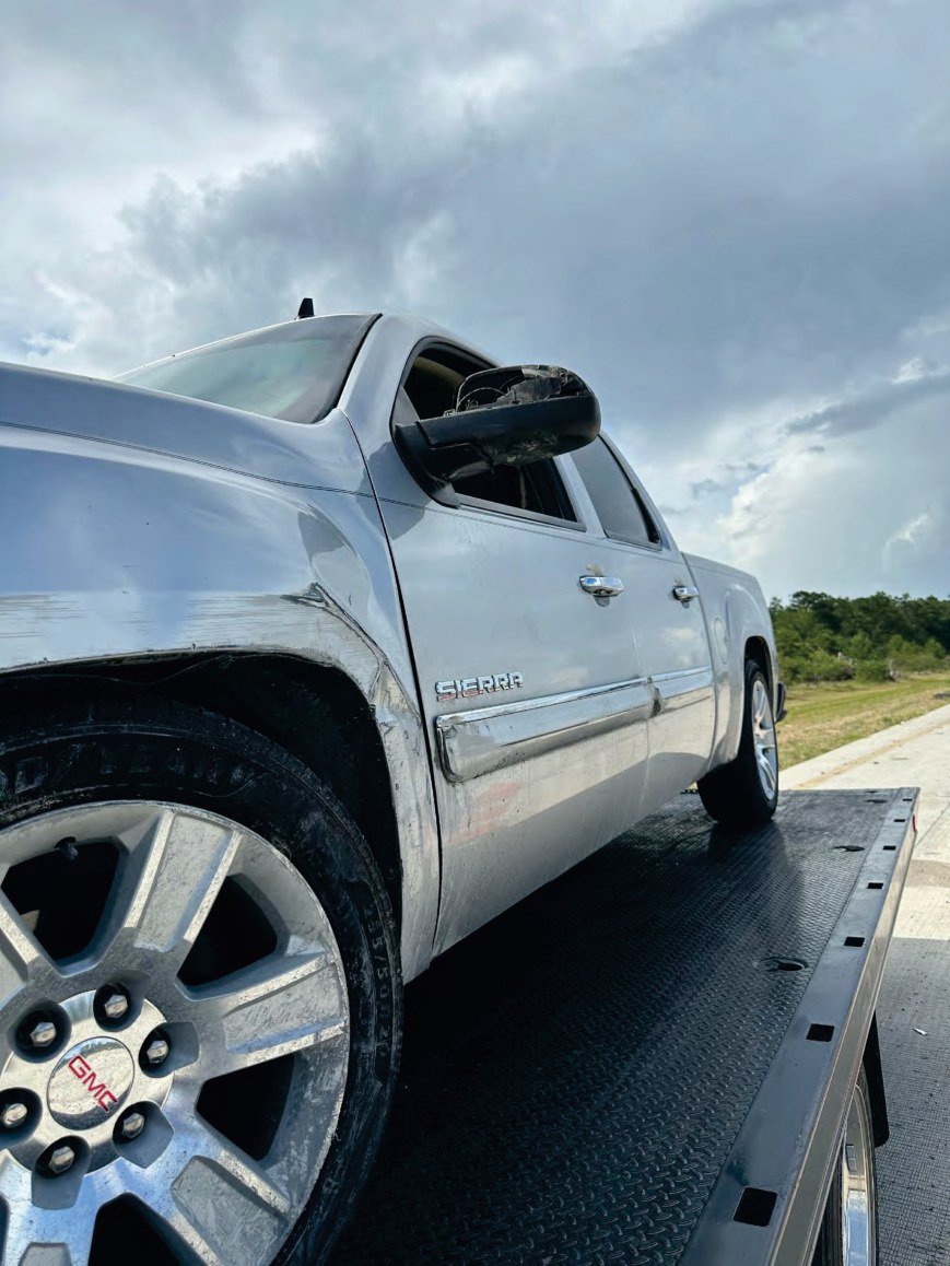 The cab of a silver pickup with a mirror torn off and a crease running down the body.